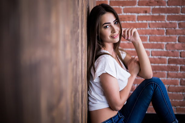Girl sitting down against wooden and brick wall - Foto, Imagen