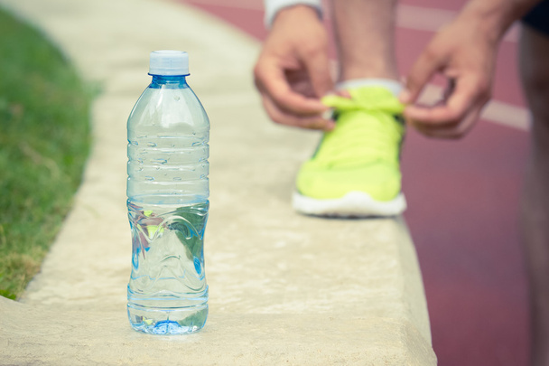 Bottle of water and hands tying shoelaces of sneaker in the background - Фото, изображение