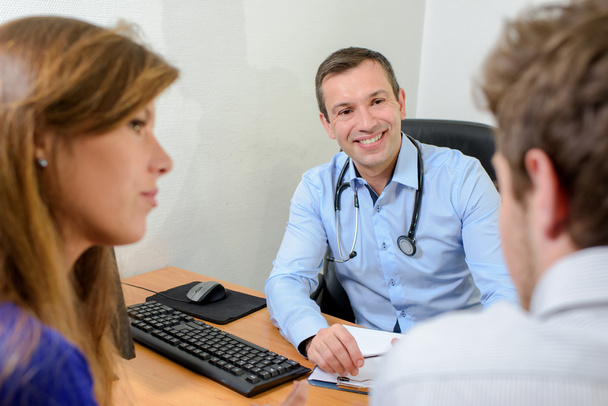 Doctor smiling at husband, wife looking cross - Photo, Image