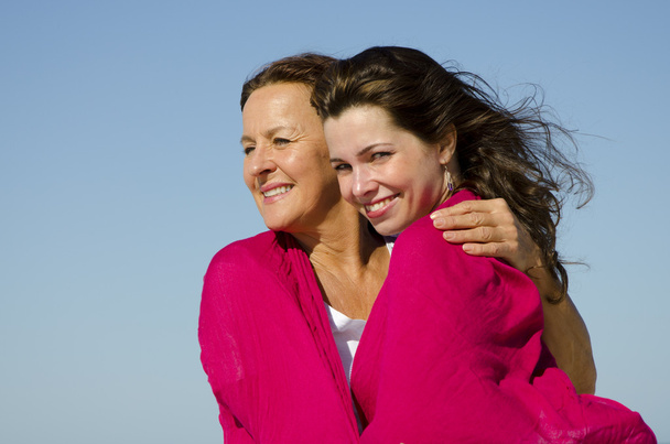 Мати обіймає дочку на відкритому повітрі в рожевому тканинному шарфі
 - Фото, зображення
