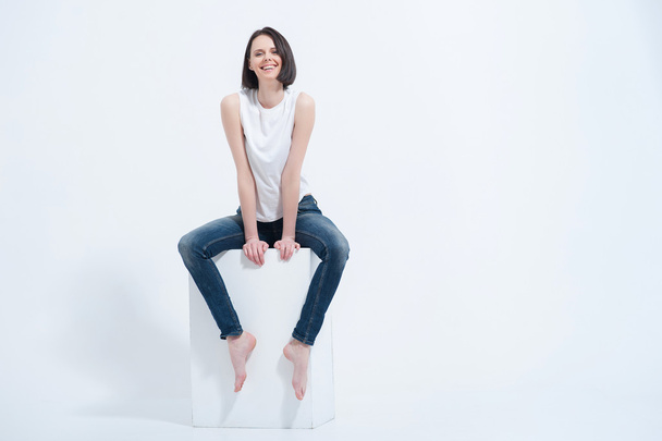 Beautiful young woman sitting on white cube in studio - Фото, зображення