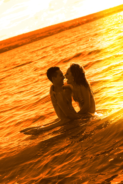 Двоє молодих дорослих коханців стоять у воді на заході сонця
  - Фото, зображення