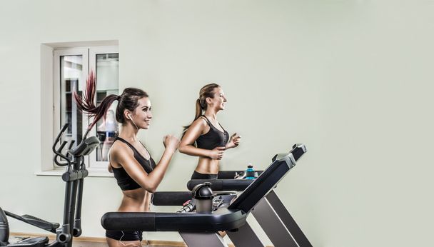 Two young sporty women running  on treadmills  in the gym - Foto, Imagen