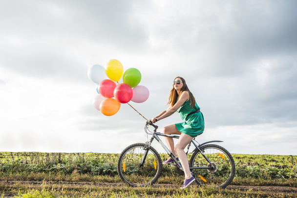 Young Girl in sexy dress  riding bicycle flying air balloons  - Zdjęcie, obraz