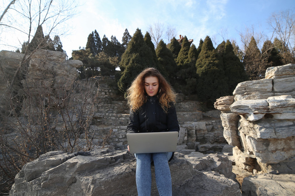 Красивая молодая девушка сидит с ноутбуком в парке на фоне гор. Интернет дает бесконечные возможности работать, учиться, общаться
. - Фото, изображение