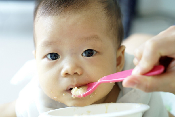 niedliches Baby isst etwas Essen mit rosa Löffel in der Hand ihrer Mutter. - Foto, Bild