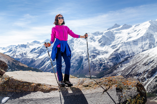 Hiker woman walking on mountain trail with hiking sticks, looking at view in Elbrus region, Caucasus mountains - Foto, afbeelding