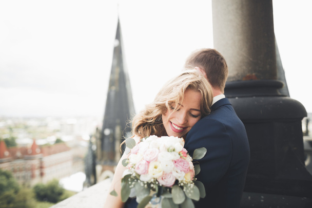 Stílusos szép esküvői pár csók és ölelés a háttérben panorámás kilátás nyílik az óvárosra - Fotó, kép