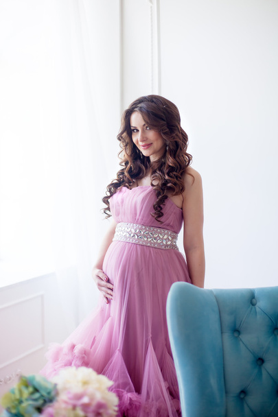 pregnancy, motherhood and expectation concept - a pregnant woman dressed in the beautiful pink evening dress smiles - Foto, Imagen