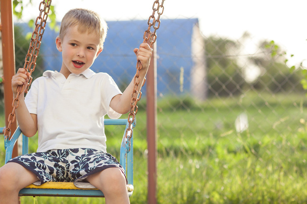 Junge spielt an sonnigem Sommertag auf Schaukeln - Foto, Bild