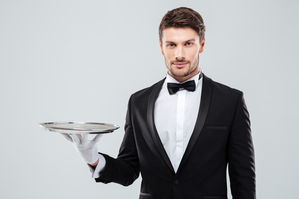 Portrait of young butler in tuxedo holding empty tray - Foto, Imagen
