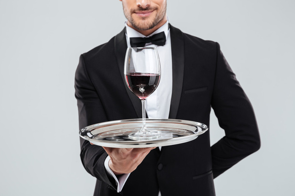 Butler in tuxedo holding silver tray with glass of wine - Photo, image
