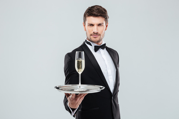 Attractive young butler in tuxedo offers you glass of champagne - 写真・画像