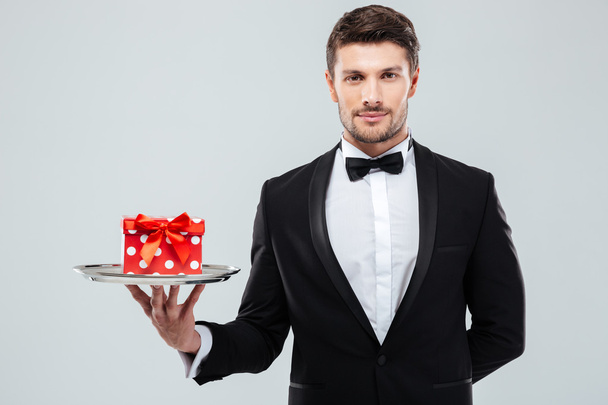 Waiter in tuxedo with bowtie holding present box on tray - Valokuva, kuva