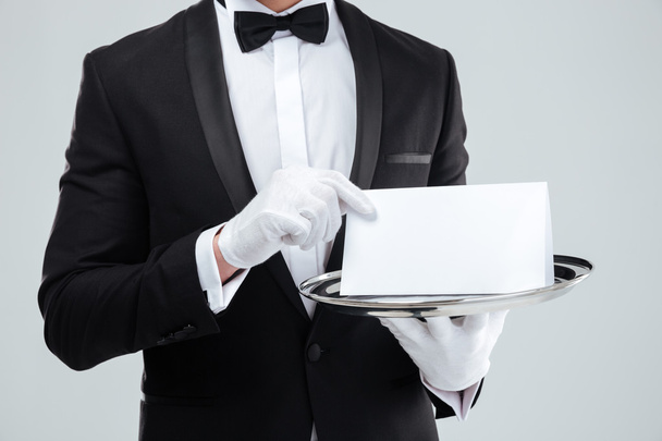 Butler in tuxedo and gloves holding blank card on tray - Fotó, kép