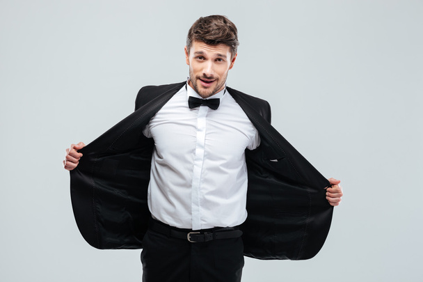 Smiling young man in tuxedo taking off his jacket - 写真・画像