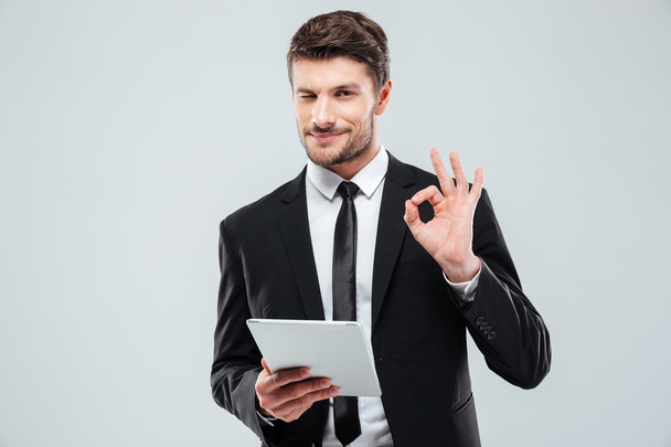 Happy young businessman with tablet winking and showing ok sign - Φωτογραφία, εικόνα