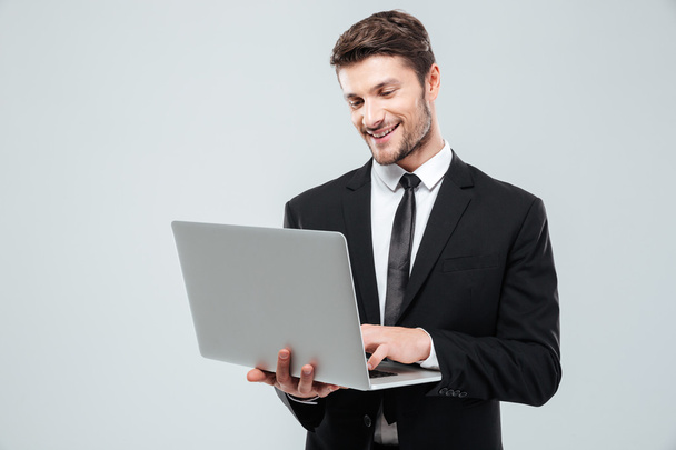 Cheerful young businessman smiling and using laptop - Foto, Imagem