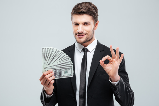 Confident young businessman holding money and showing ok sign - Photo, Image