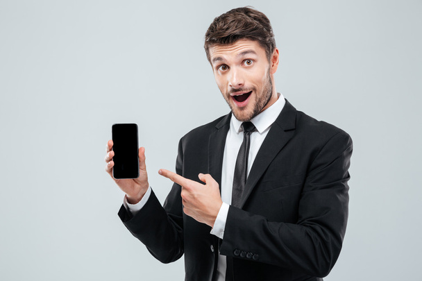 Amazed young businessman holding and pointing on blank screen smartphone - Foto, afbeelding