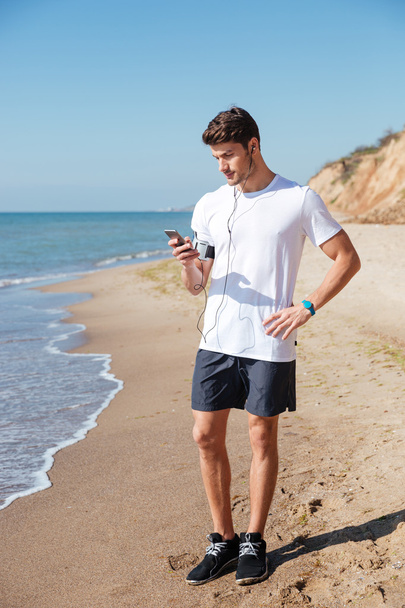 Sportsman listening to music using cell phone on the beach - Photo, Image