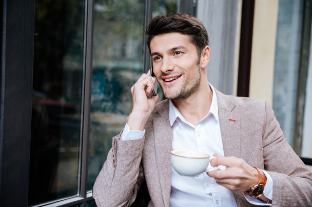 Smiling young businessman talking on mobile phone in outdoor cafe - Foto, afbeelding
