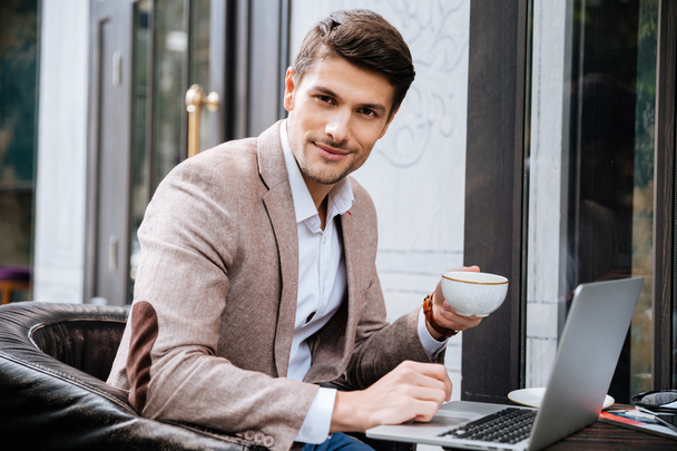 Man with laptop sitting and drinking coffee in outdoor cafe - Foto, imagen