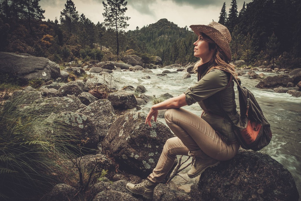 Kaunis nainen vaellus istuu kiven lähellä Wild Mountain River
. - Valokuva, kuva