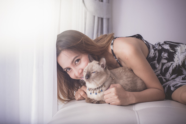 Asian woman and cat laying on sofa with window light. - Foto, Imagen