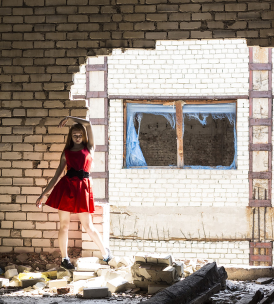 破壊された建物の壁の背景に赤いドレスでそばかすの赤毛の細いスリムな女の子 - 写真・画像