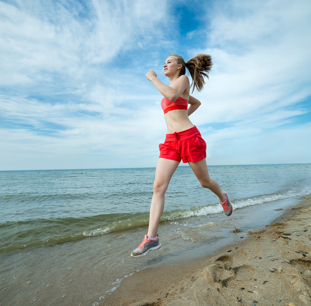 Young lady running at the sunny summer sand beach. Workout.  Jog - Zdjęcie, obraz
