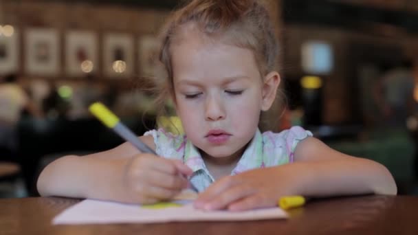 little girl draws in the cafe waiting for the order. child in restaurant - Footage, Video