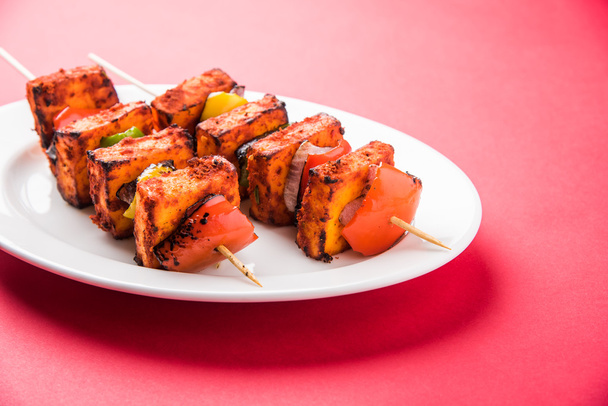 Paneer Tikka Kabab - Tandoori Indian cheese skewers, malai paneer tikka / malai paneer kabab, chilli paneer served in white plate with barbecue stick and colourful capsicum and onion, with green sauce - Photo, Image