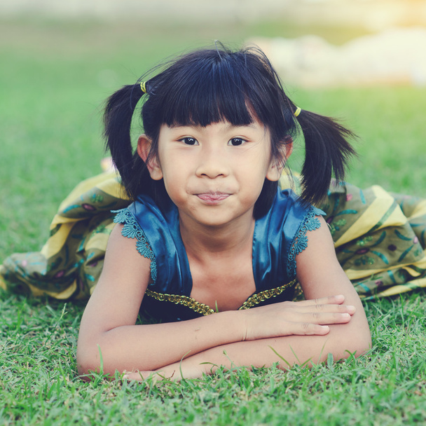 Asian girl in princess dress lying on grass and looking at camer - 写真・画像