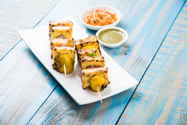 Paneer Tikka Kabab - Tandoori Indian cheese skewers, malai paneer tikka / malai paneer kabab, chilli paneer served in white plate with barbecue stick and green sauce, selective focus - Photo, Image