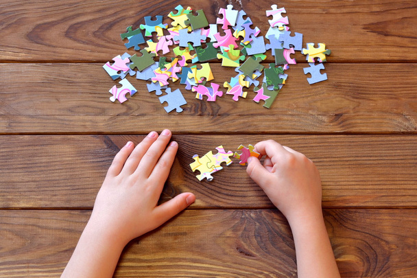 Kinderpuzzels in de hand houden. Een set kleurrijke legpuzzelstukjes op houten tafel. Kinderen handen proberen legpuzzelstukjes met elkaar te verbinden. Jig zag puzzelspel oplossingen concept. Kinderen mind games - Foto, afbeelding