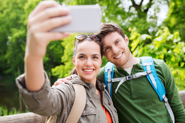 couple with backpacks taking selfie by smartphone - Foto, afbeelding