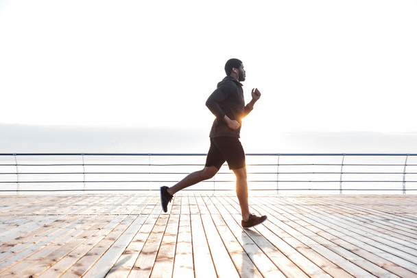 Handsome african american young sportsman running on pier - Zdjęcie, obraz