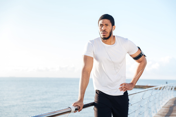 Sportsman listening to music using earphones standing on pier - Foto, Imagem