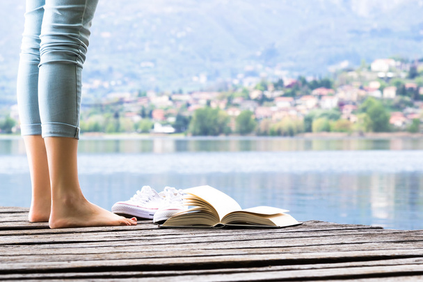Νεαρή κοπέλα ψέματα σχετικά με μια προβλήτα και ένα βιβλίο στα γυμνά πόδια - Φωτογραφία, εικόνα