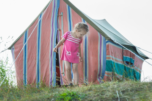 Маленькая девочка, стоящая возле полосатой винтажной палатки для кемпинга
 - Фото, изображение