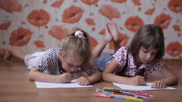 Giovani gemelle sorelle stanno disegnando su carta con matite colorate sdraiate sul pavimento
. - Filmati, video