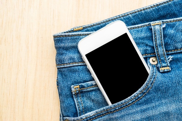 Telefon komórkowy w niebieskie dżinsy spodnie na tle drewna - Zdjęcie, obraz