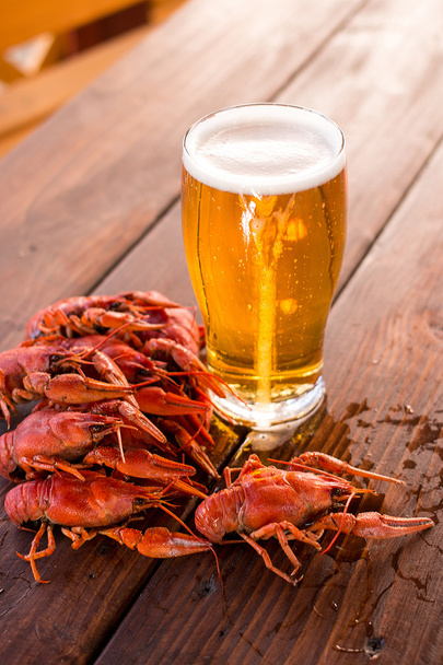 Copo cheio de cerveja com lagosta fervida na mesa
 - Foto, Imagem