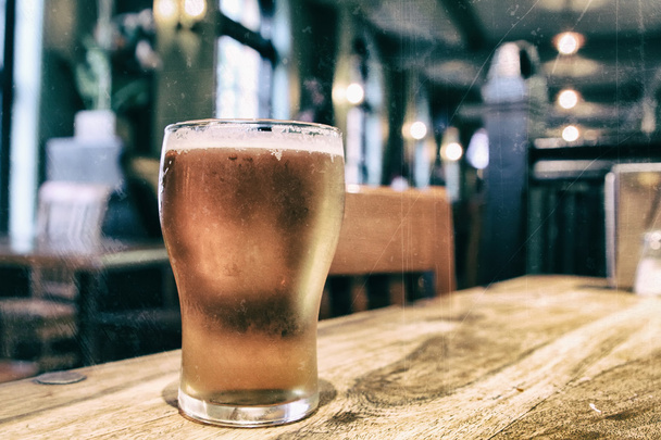 Nahaufnahme eines Glases frisches schäumendes Bier auf einem Tisch in einem Vintage-Weichzeichner - Foto, Bild