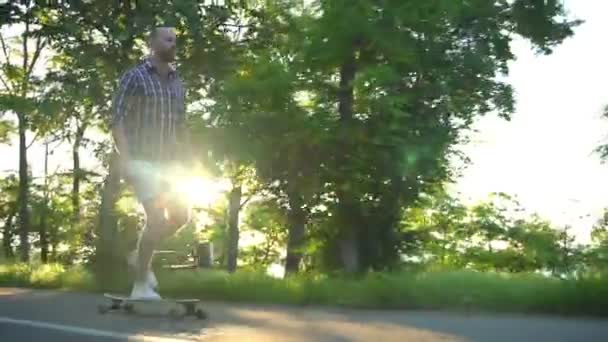 jóképű férfi lovaglás longboard parkban a napsütéses napon lassú mozgás - Felvétel, videó