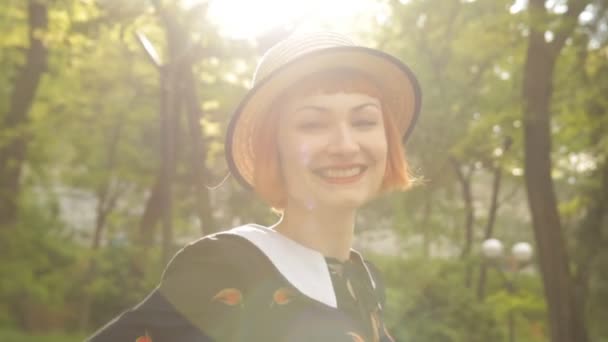 Beautiful redhead young woman blowing kiss, smiling, flirting. Attractive and cheerful pin-up girl in a retro style dress and hat. Positive emotions. Happy and joyful. Sunset. Slow motion. - Footage, Video