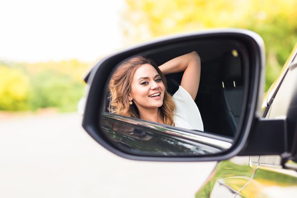 Boldog fiatal nő vezető keres az autó oldalán tükör. Kirándulás, utazás, vezetői koncepció - Fotó, kép