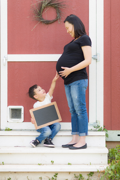 Hijo con pizarra en blanco apuntando a la barriga embarazada de mamá
 - Foto, Imagen