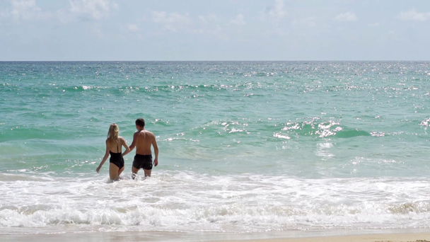 Loving couple on the beach holding hands and goes into the water - Materiał filmowy, wideo